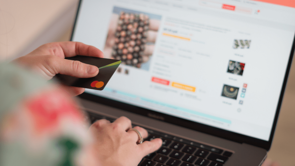 A person holding a credit card in front of a laptop.