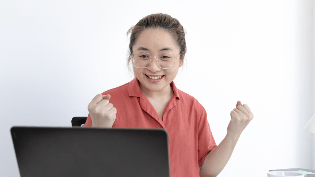 A person is sitting in front of a laptop with their hands up.
