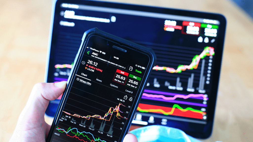 A person using their smartphone to view stock market data on their laptop.