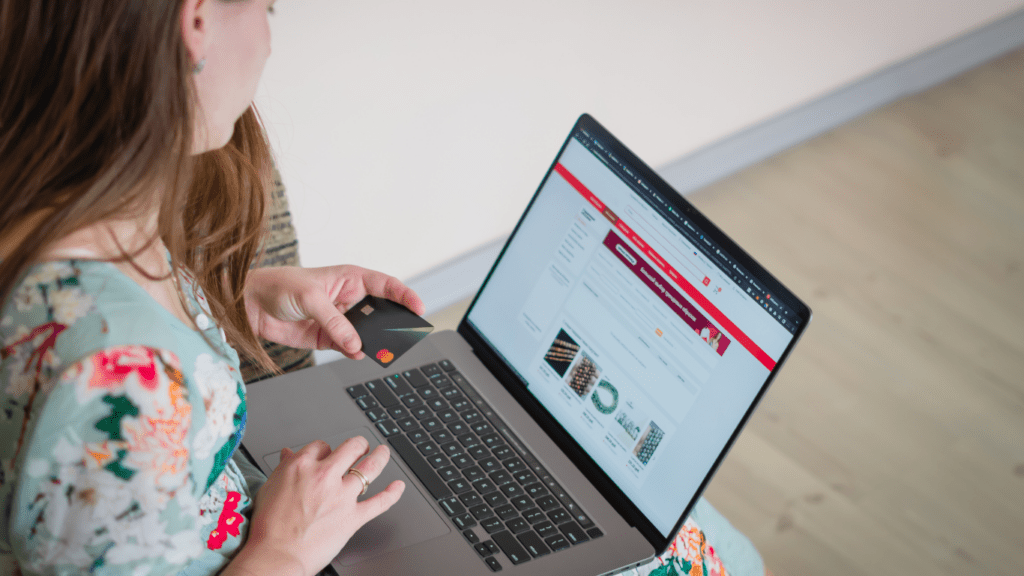 A person holding a credit card in front of a laptop.
