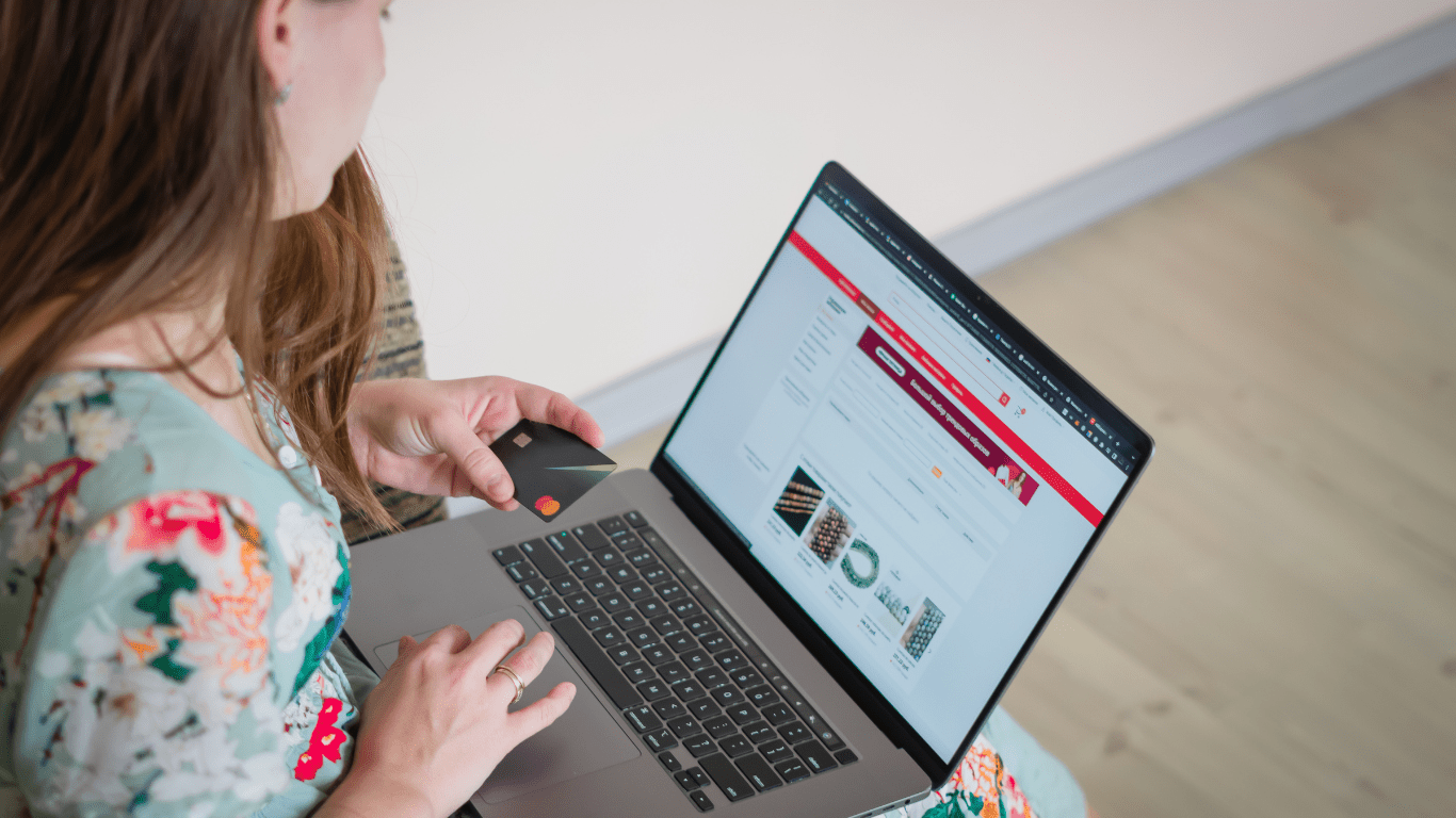 A person holding a credit card in front of a laptop.
